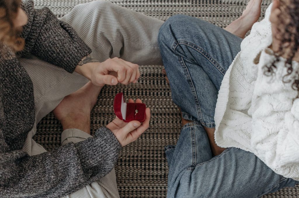 Guy proposing intimately at home with red box and engagement ring